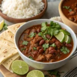 A hearty bowl of pinto beans with chorizo, garnished with fresh cilantro and lime wedges, served next to warm tortillas or rice.