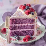 A beautifully frosted purple velvet cake with white buttercream, topped with fresh raspberries, blueberries, and edible glitter, served with a slice on a decorative plate.